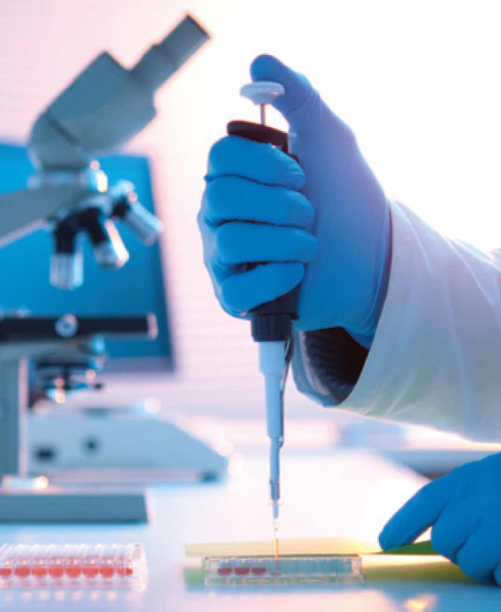 A laboratory professional using a pipette beside a microscope